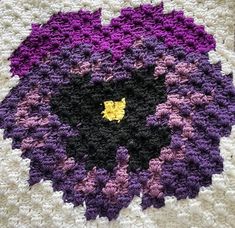 a crocheted square with a yellow flower in the center and purple flowers on it