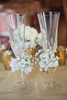 two wine glasses with flowers in them sitting on a table next to gold vases