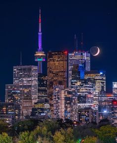 the city skyline is lit up at night with bright lights and moon in the sky