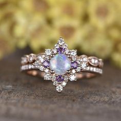 an opal and diamond ring on top of a wooden table with flowers in the background