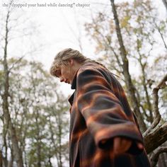 a man standing in the woods looking down at his cell phone while wearing a blanket