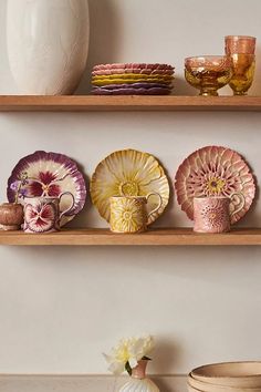 three wooden shelves with plates and cups on them next to a vase, bowl and other items