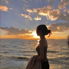 a woman standing on top of a sandy beach next to the ocean at sun set