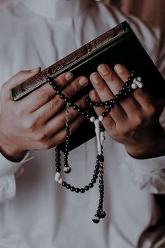 a man in white shirt holding rosary and book with both hands on the bible cover