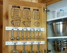 a wooden cabinet with measuring spoons and measuring cups on the bottom, labeled kitchen utensils