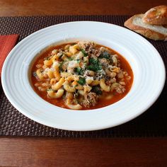 a bowl of pasta soup with bread on the side