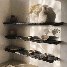 three black shelves with vases and bowls on them in the corner of a room