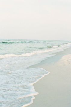 a person walking on the beach with a surfboard in their hand and waves coming in to shore