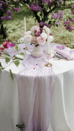 a table with flowers and candles on it in the middle of a field, surrounded by trees