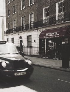 a black and white photo of a taxi driving down the street in front of a building