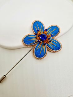 a blue and yellow flower pin sitting on top of a white plate