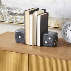 a clock and some books are sitting on a dresser next to a bookend with two dices