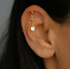 a close up of a person's ear with a gold chain and heart charm on it