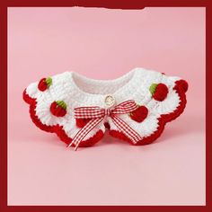 a crocheted sweater with strawberrys and bows on the collar is displayed against a pink background