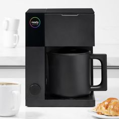 a black coffee mug sitting on top of a counter next to a white plate