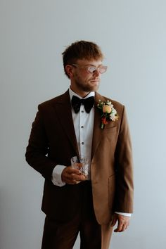 a man in a tuxedo and bow tie holding a glass with something on it