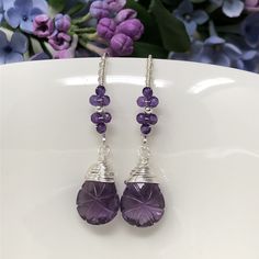 The Wisteria Path earrings weave a delicate story of rich blooms and delicate petals. These earrings feature beautiful, tender purple amethyst that have been intricately hand-carved with a unique starburst pattern and wrapped with fine sterling silver. Gracefully suspended from marquise French ear wires that are embellished with blossoms of petite, micro-faceted amethyst. Swirled, vine-like detailing on the ear wires give an extra feminine touch to these lovelies. Very lightweight, unique and oh Lavender Amethyst Earrings With Natural Stones, Elegant Purple Wire Wrapped Crystal Earrings, Nickel-free Purple Briolette Earrings, Lavender Amethyst Earrings With Ear Wire, Purple Long Drop Earrings With Natural Stones, Lavender Amethyst Teardrop Earrings, Lavender Amethyst Drop Earrings, Teardrop Purple Earrings With Natural Stones, Purple Teardrop Earrings With Natural Stones