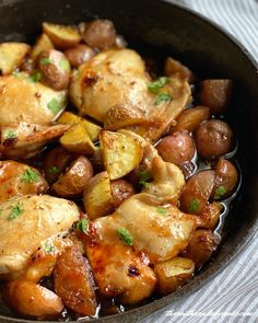 a pan filled with chicken and potatoes on top of a table