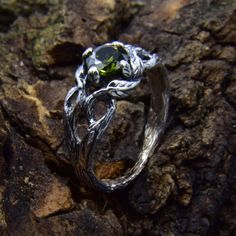 a silver ring sitting on top of a rock covered in leaves and stones with a green stone