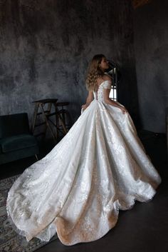 a woman in a white wedding dress is standing near a couch and looking at the wall