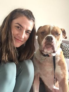 a woman sitting on a couch next to a brown and white pitbull dog