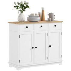 a white cabinet with drawers and plates on the counter top next to a vase filled with flowers