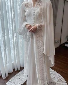 a woman wearing a white dress and cape standing in front of a window with curtains