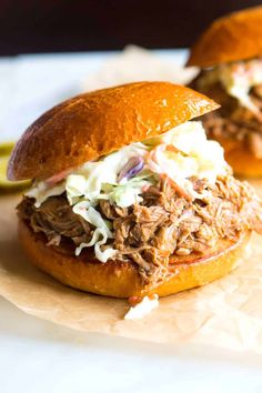 two pulled pork sandwiches with cole slaw on top are sitting on wax paper next to a banana