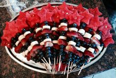 a platter filled with fruit and veggies on skewers next to watermelon wedges