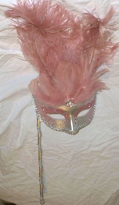 a masquerade with pink feathers on top of a white sheeted bed cover