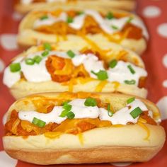 three hot dogs covered in cheese and onions on a red tablecloth with white polka dots