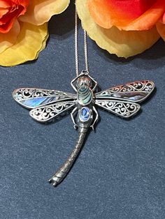 a dragonfly pendant is sitting on a table next to some flowers and orange roses