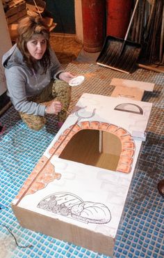 a woman kneeling on the floor next to a cardboard box that is cut out and painted