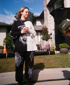 a woman standing in front of a house holding a cup and talking to another person