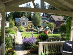 people are gathered in the back yard of a house with lots of plants and flowers