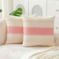 two pillows sitting on top of a white couch next to a green potted plant