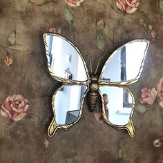 a butterfly shaped mirror sitting on top of a table next to a flower covered wall