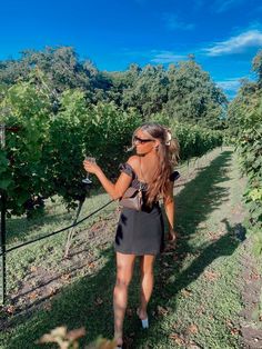 a woman in a short dress is walking through the vineyard