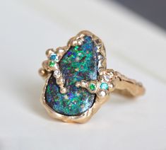 "Our one-of-a-kind 14k yellow gold boulder-opal ring celebrates the natural beauty of this incredible gemstone with a gracefully undulating branch band and hand-hammered texture that emphasizes it's slightly rustic nature: organic minimalism with a brutalist vibe. It's designed to stand on its own as a unique statement, but it also plays well with other pieces adding texture to your daily ring stack. The companion stones, diamond, blue topaz and tsavorite garnet, play to the galactic color of th Organic Minimalism, Boulder Opal Ring, Mode Kimono, Branch Ring, Tsavorite Garnet, Organic Style, Ring Stack, Raw Beauty, Hammered Gold