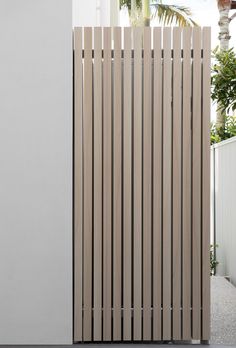 a tall wooden slatted fence next to a white wall and potted plant