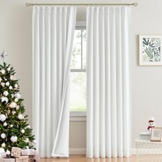 a christmas tree in front of a window with white curtains