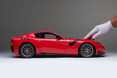 a person in white gloves is touching a red sports car