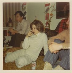 two men and a woman sitting on the floor in a living room, one holding a cell phone to her ear