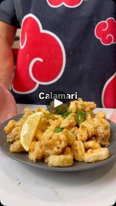 a plate full of fried food with lemon wedges on the side next to a person