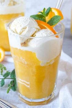 two glasses filled with ice cream, orange slices and mint garnish on a white cloth