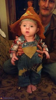 a man holding a baby wearing a scarecrow hat