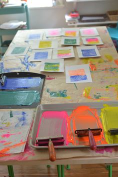 the table is covered with many different colored papers and paintbrushes, including watercolors