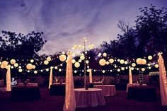 an outdoor wedding setup with lanterns and tablecloths on the ground at night time