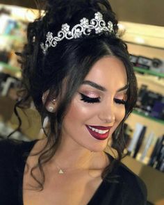 a woman wearing a tiara and makeup looks down at her cell phone while smiling