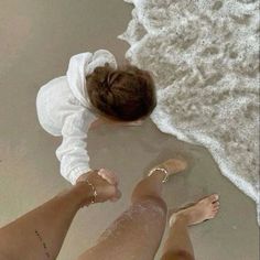 two people standing on the beach with their feet in the water and one is wearing a white shirt